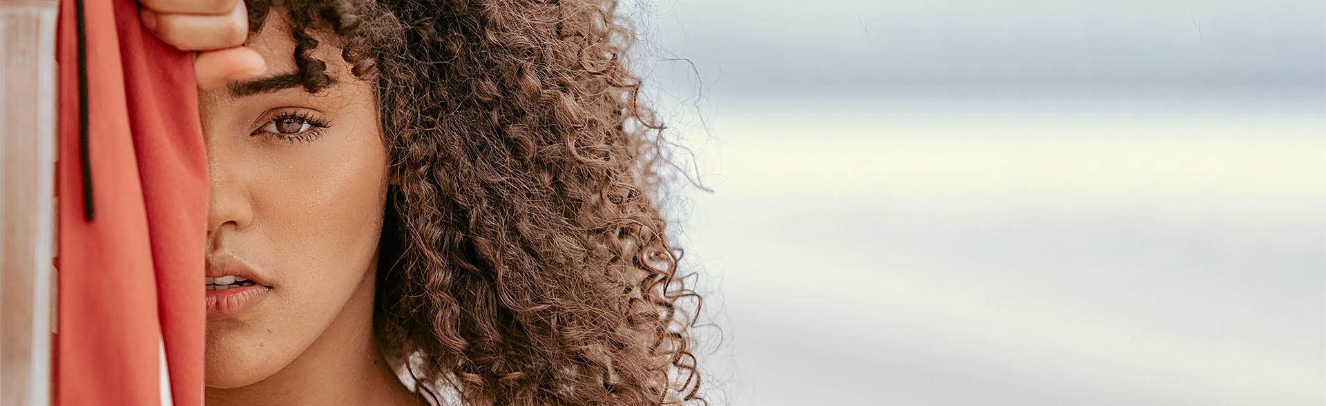 Frau mit lockigen braunen Haaren hält ein rotes Tuch vor ihr Gesicht.